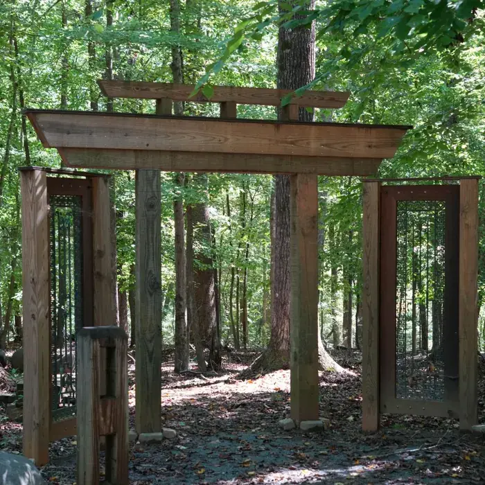A tall timber gate standing among the trees, with panelled doors either side of it.