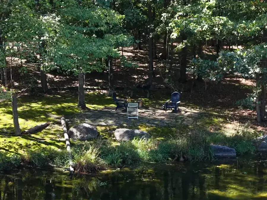 Chairs set out on a stone patio at the edge of the pond, seen from across the water.